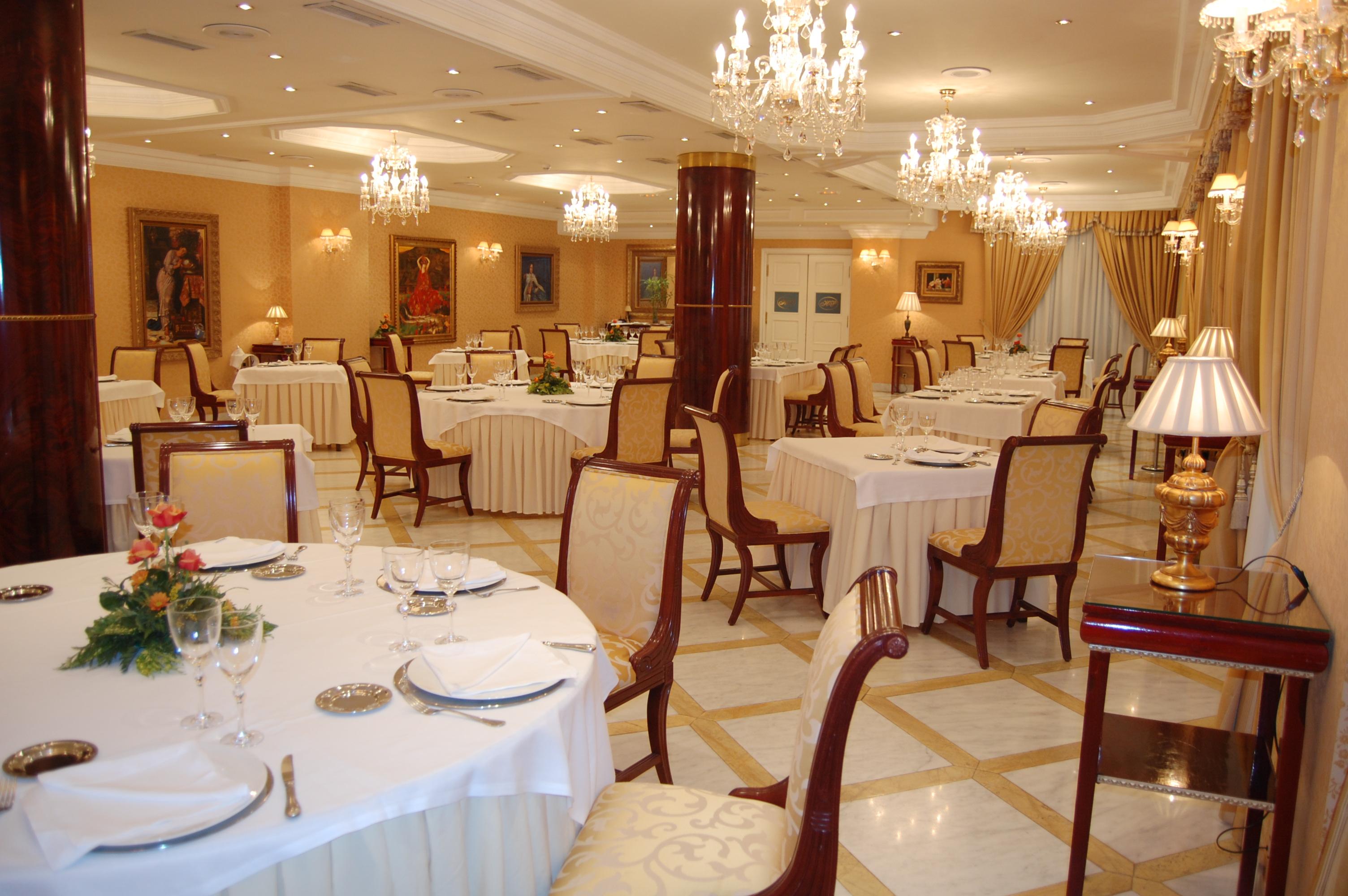 Hotel Alameda Palace Саламанка Ресторан фото The photo shows an elegant dining restaurant. The interior features well-set tables with white tablecloths and finely arranged place settings, including plates, glasses, and silverware. The chairs are ornate and styled, reflecting a sophisticated amb