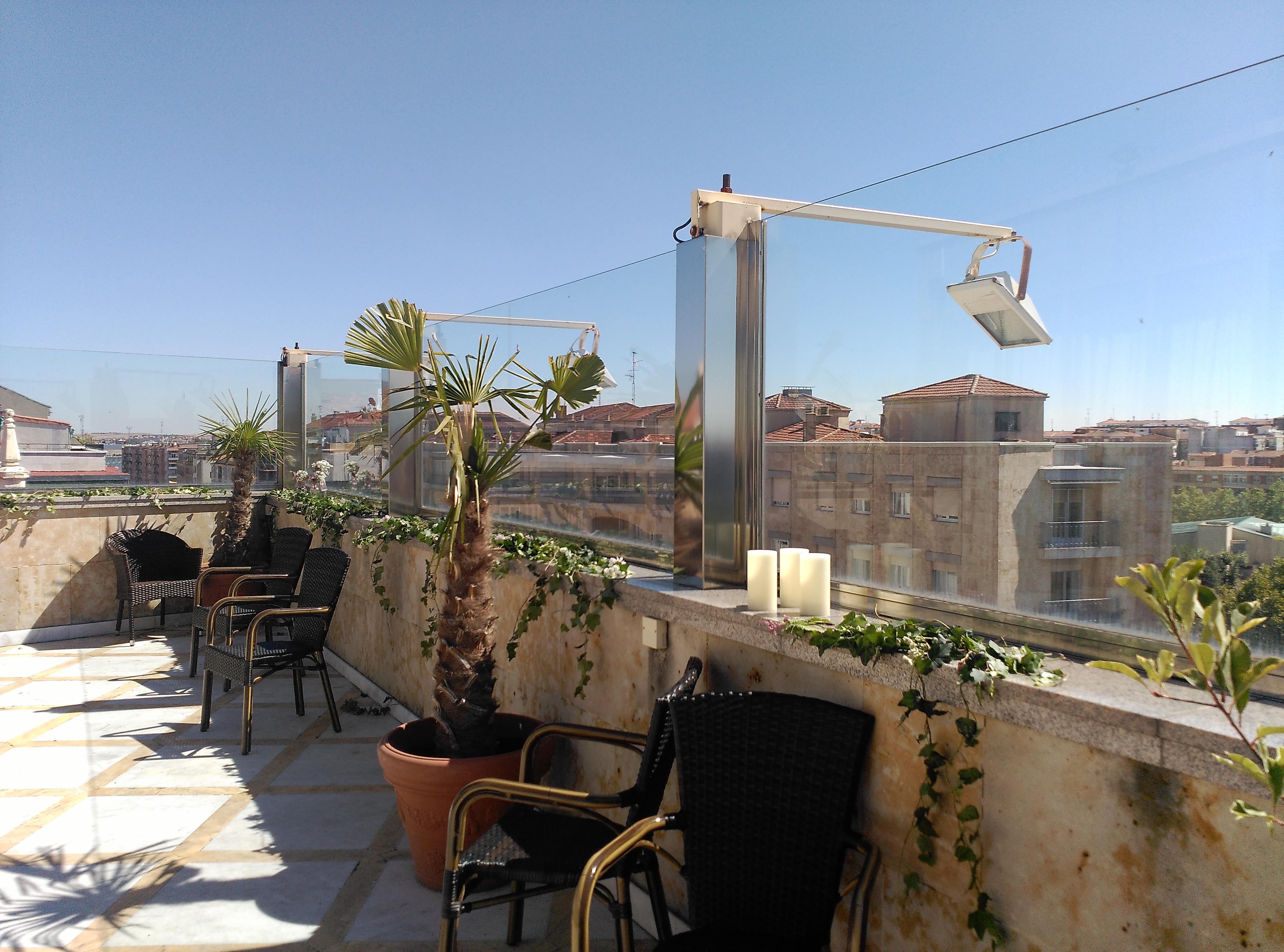 Hotel Alameda Palace Саламанка Экстерьер фото The photo shows a rooftop terrace featuring a sunny environment. There are several chairs arranged on the terrace, along with potted plants, including palm-like greenery. The terrace has clear glass panels that provide a view of the surrounding build