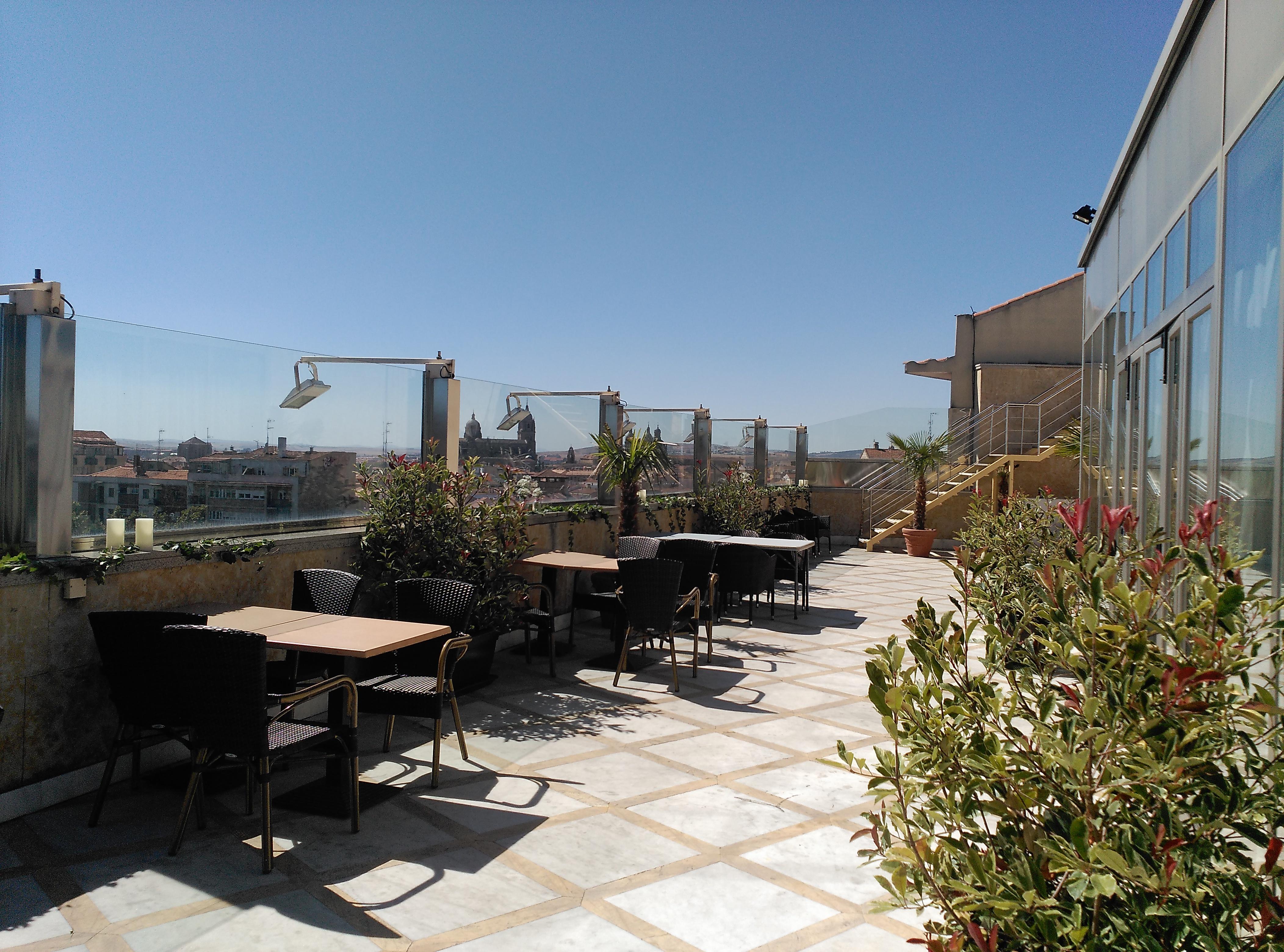 Hotel Alameda Palace Саламанка Экстерьер фото The photo shows a rooftop terrace with several outdoor tables and chairs arranged in different areas. The floor appears to be tiled, and there are some plants in pots adding greenery to the space. In the background, there are cityscapes visible under