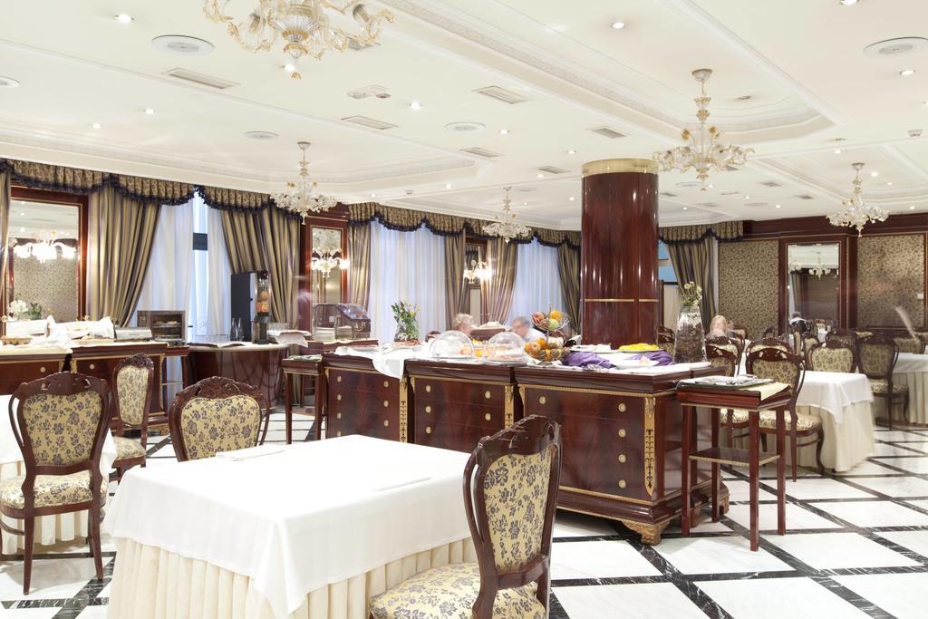 Hotel Alameda Palace Саламанка Экстерьер фото The photo depicts an elegant dining area or restaurant. It features several tables covered with white tablecloths and surrounded by ornate chairs. The room has a classic design with decorative curtains and chandeliers hanging from the ceiling. In the